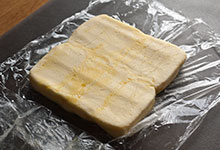 A block of butter pounded into a square on plastic wrap